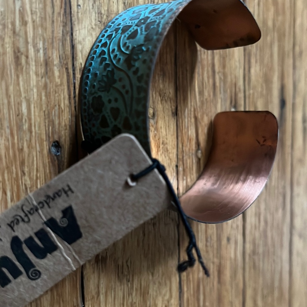 Copper bracelet with raised relief and turquoise patina floral motif.